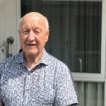 An elderly male, standing outside his home.