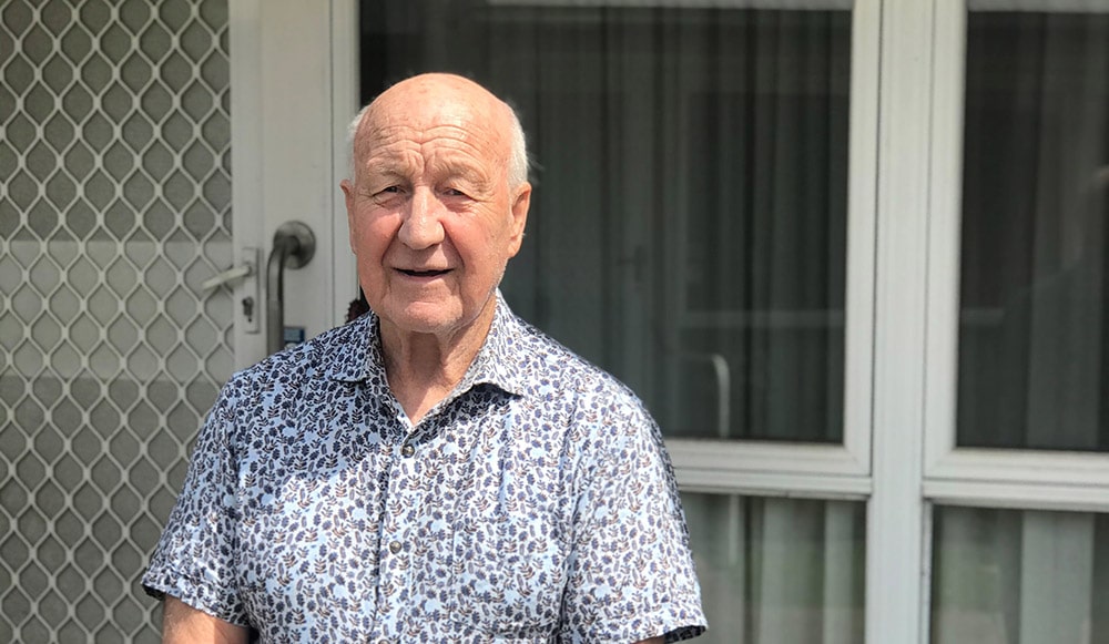 An elderly male, standing outside his home.