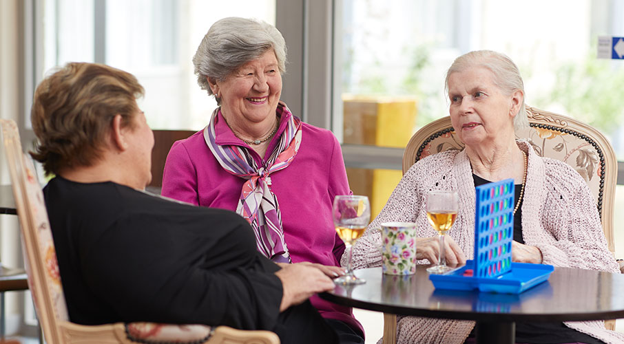 Three elderly woman laughing together, while playing a board game