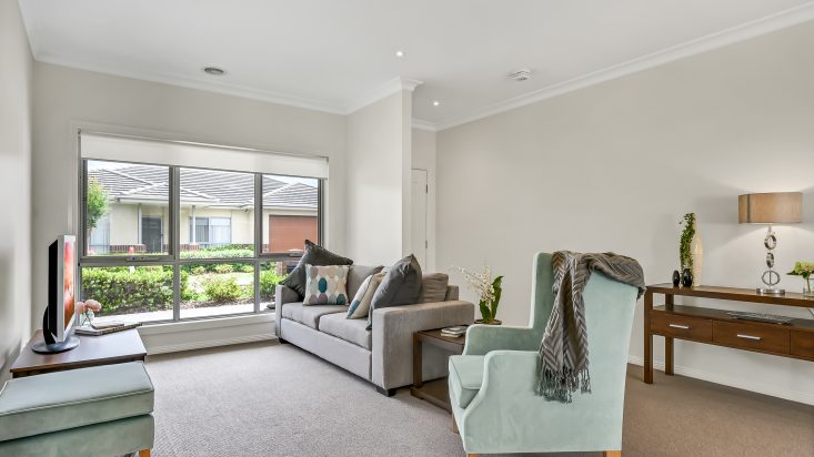 Grey couch and light blue armchair in grey carpeted room, large window opens the room to the street