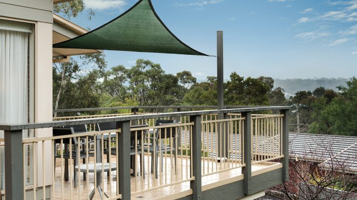 Balcony with cream flooring and dining set on a sunny day, a green shade provides cover