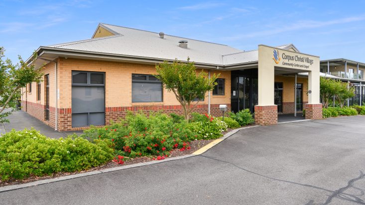 Large red brick and yellow building, trees and bushes are growing in the front garden