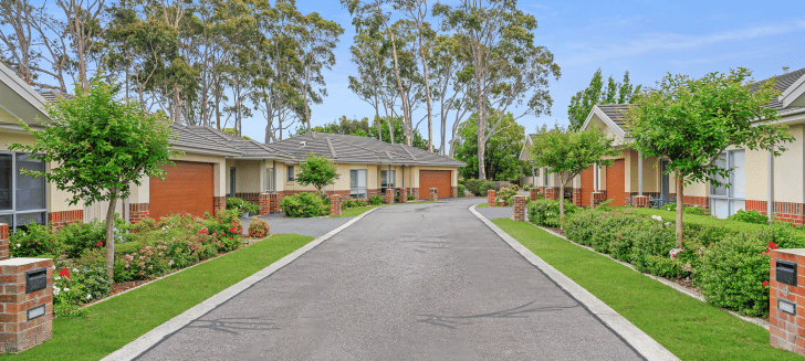 View down a tree lined street, houses are brick and cream coloured with red-brown garages