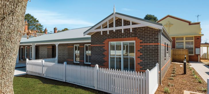 Brown brick home with a white picket fence, red brick details the front window