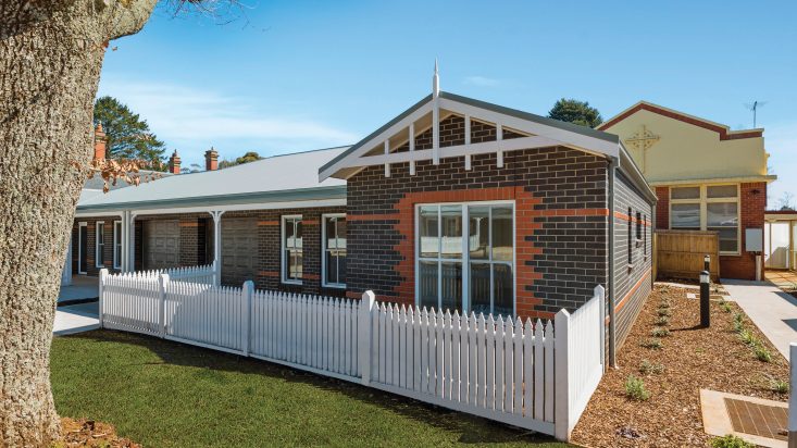 Brown brick home with a white picket fence, red brick details the front window