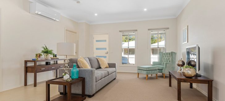 Living room with beige carpet, a grey couch and light blue armchair and ottoman sit next to wooden side tables