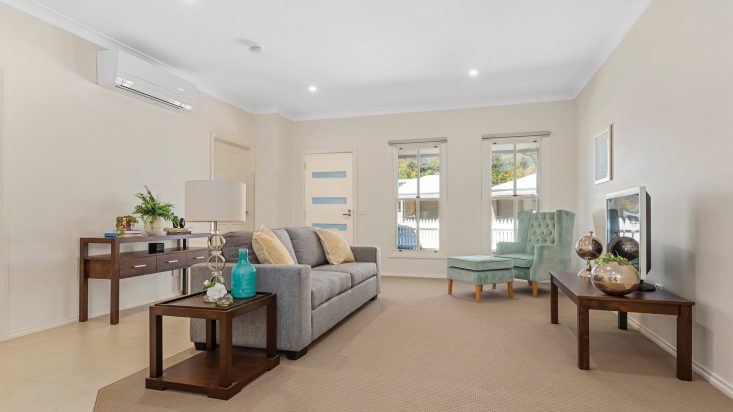 Living room with beige carpet, a grey couch and light blue armchair and ottoman sit next to wooden side tables