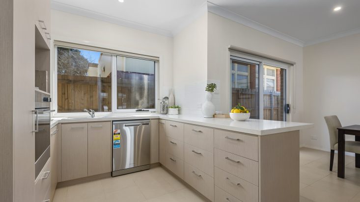 U-shaped kitchen with grey beige cabinets and white benchtop, a window sits above the sink