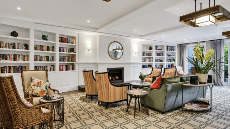 Dark green velvet lounge and armchairs sit around a built-fireplace, built in bookshelf on either side