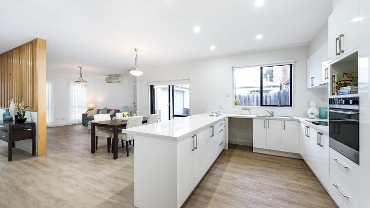 U shaped kitchen with white benchtop, dining and lounge room in background.