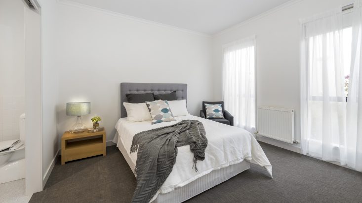 Bedroom with dark grey carpet, double bed with a wooden bedside table and grey armchair.