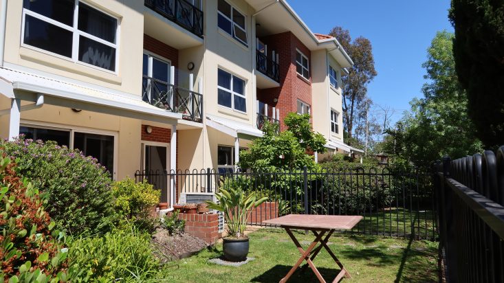 Front ground level courtyard with green grass and wooden table, three story brick building behind