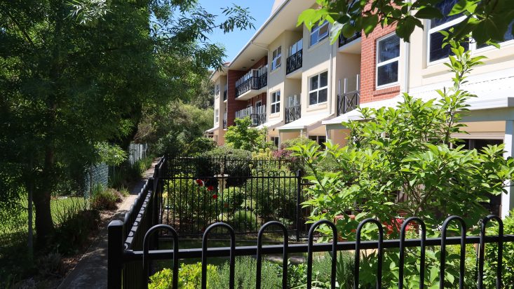 Black metal fence around courtyards with shrubs and trees, brick apartments behind