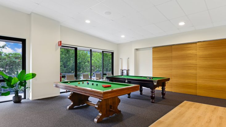 Two pool tables with walnut bases sit on carpet, window behind