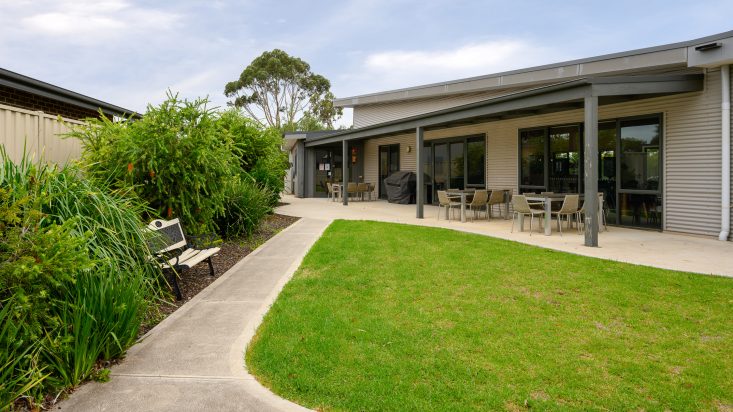 Lawn in front of outside dining sets that are sitting underneath a patio cover