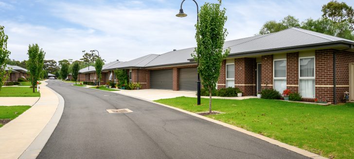 Rows of brown brick houses with grey metal roofs, lamppost and tree in front yard