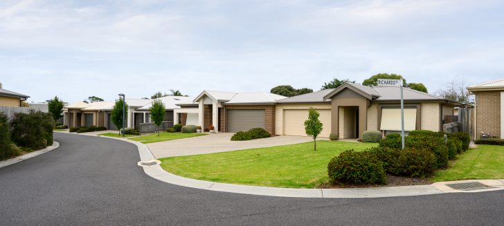 Beige, brick and cream houses with front gardens and shrubs, street in foreground.