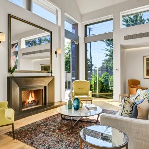 Grey lounge and yellow armchairs around a metal fireplace, tall windows on adjacent walls