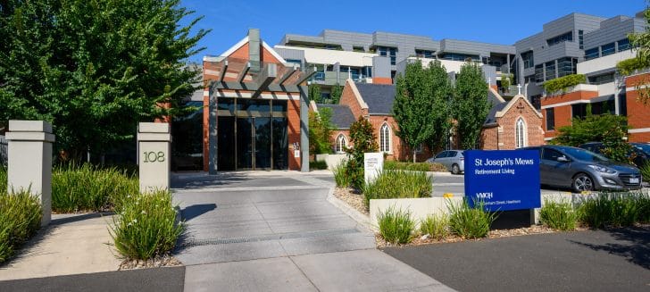 Driveway and car parking in front of a large brick building, red brick church sits beside