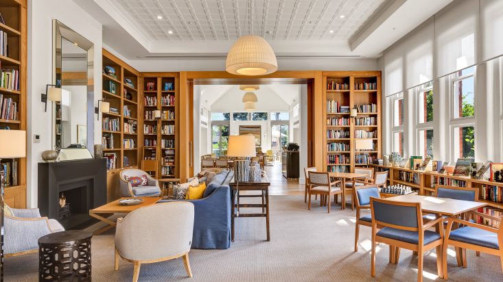 A cathedral style room with high ceilings with dining sets and a lounge area. A wooden bookshelf is built into the walls.