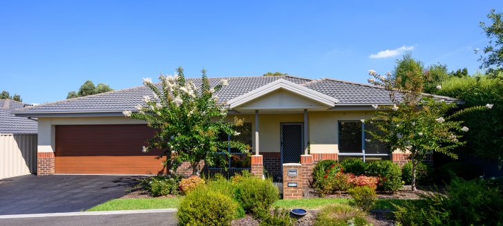 A cream house with red bricks half way up, shrubs and trees in the front garden