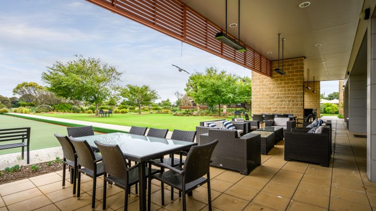 Outdoor dining sets underneath the patio with ceiling mounted heaters. View out to grass and trees.