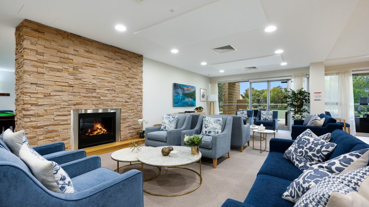 Blue arm chairs and couch circle around two marble coffee tables with gold legs. A gas fireplace sits in the wall behind the coffee table.