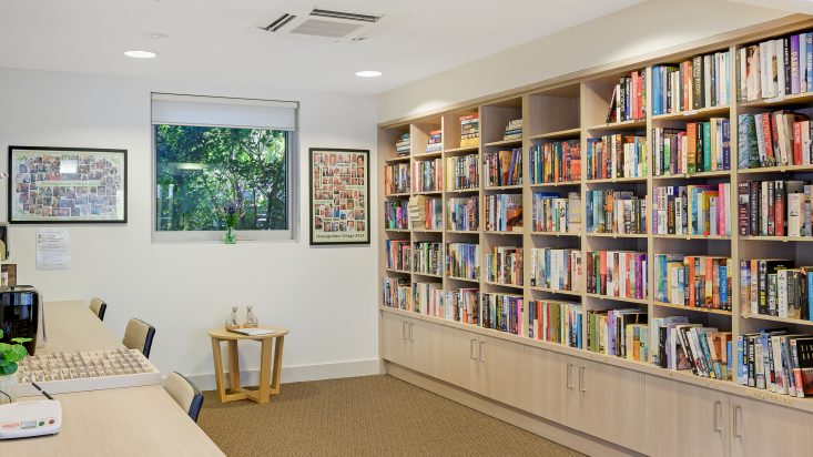 Desk on left wall, wooden built in bookshelf is filled with colourful books on the opposite wall