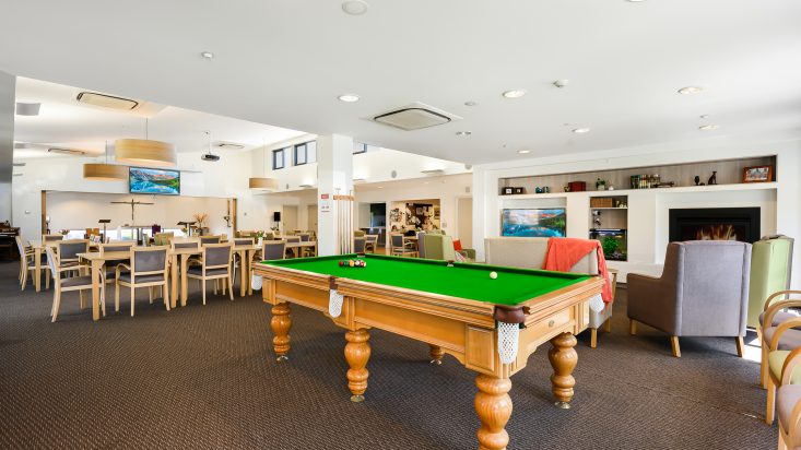 Pool table with wooden base, community centre lounge and dining area can be seen behind