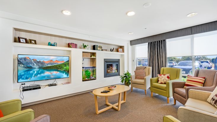 Green and gray armchairs circle a wooden coffee table, fireplace and tv on adjacent wall