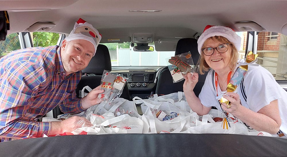 A man and a woman in a car, wearing Christmas hats and holding products from the Christmas Hampers