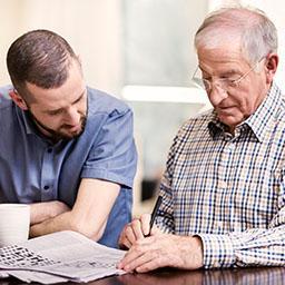 Elderly man doing the crossword with man in scrubs