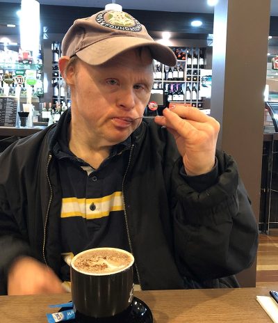 A man wearing a cap and dark jacket sips his coffee