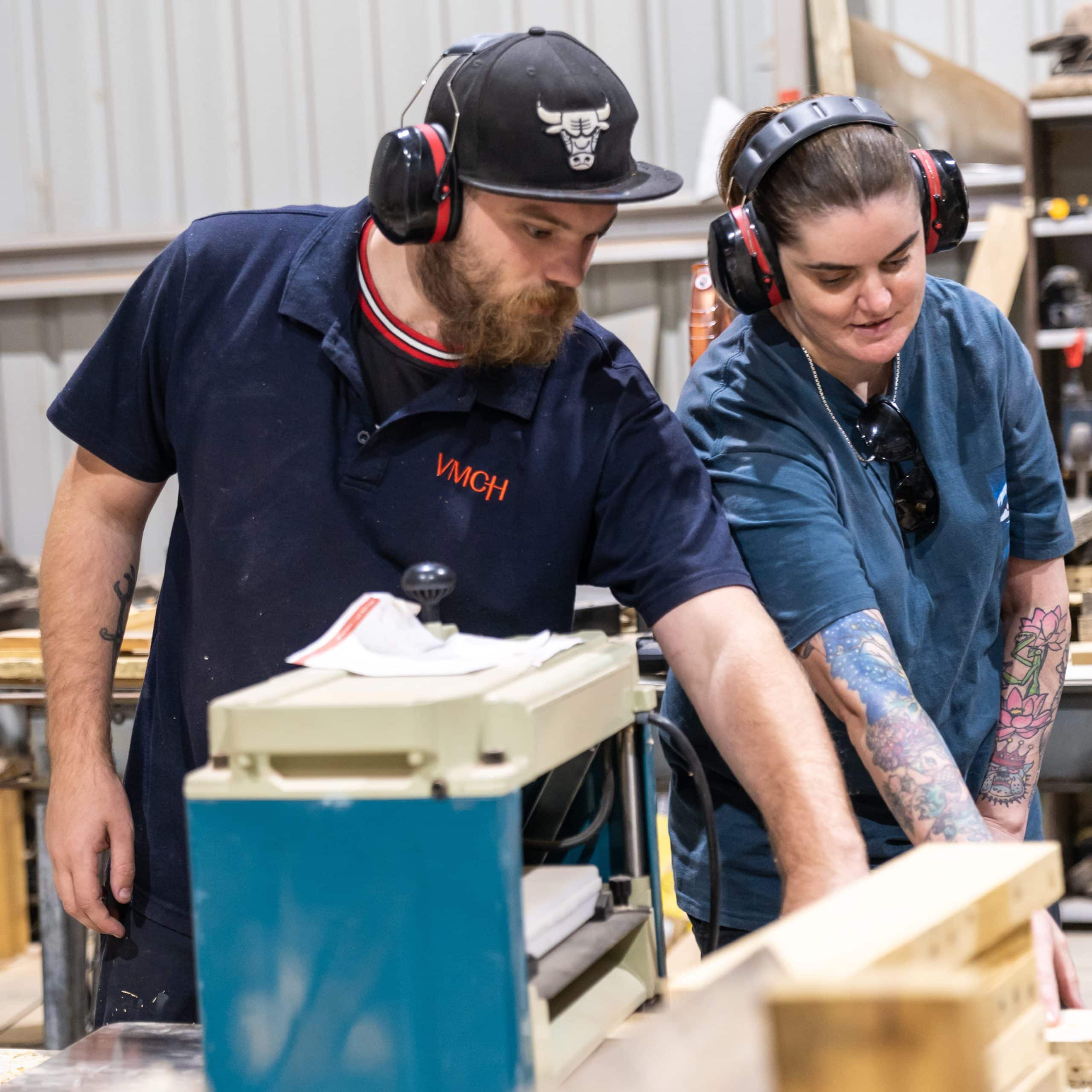 A man and woman using tools within a woodworking shed