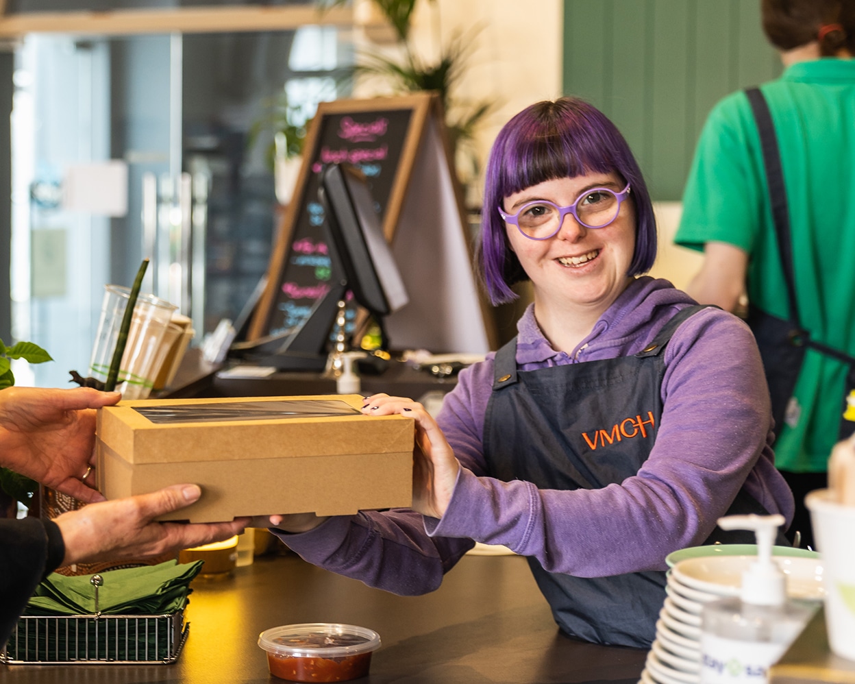 Female cafe worker, handing over a box of food while smiling