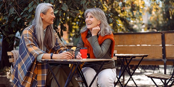 Two women sitting at a table together, drinking coffee and laughing