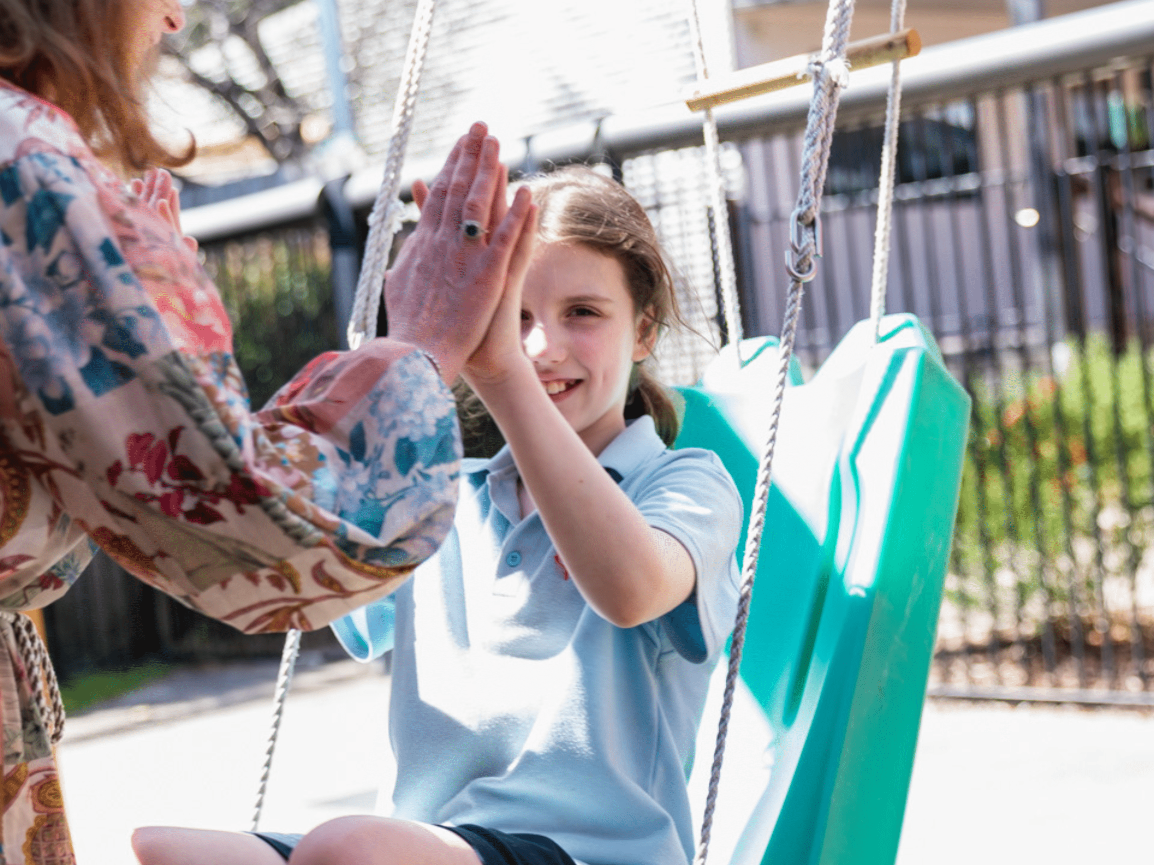 A girl on a swing high fives a woman