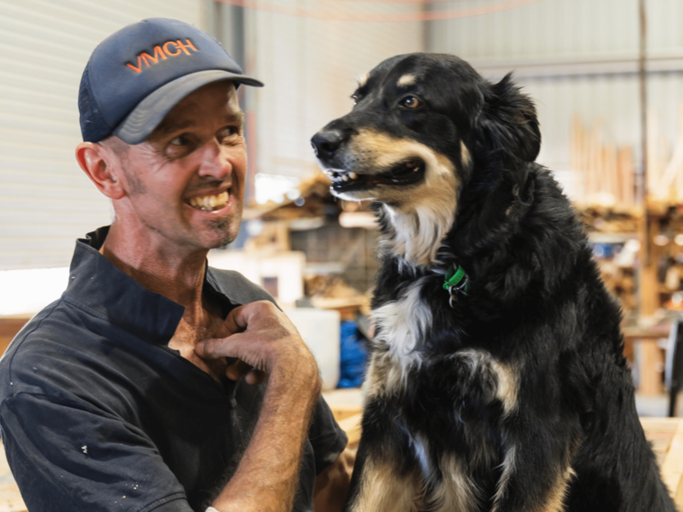 A man in a cap smiles at a black and caramel coloured dog.