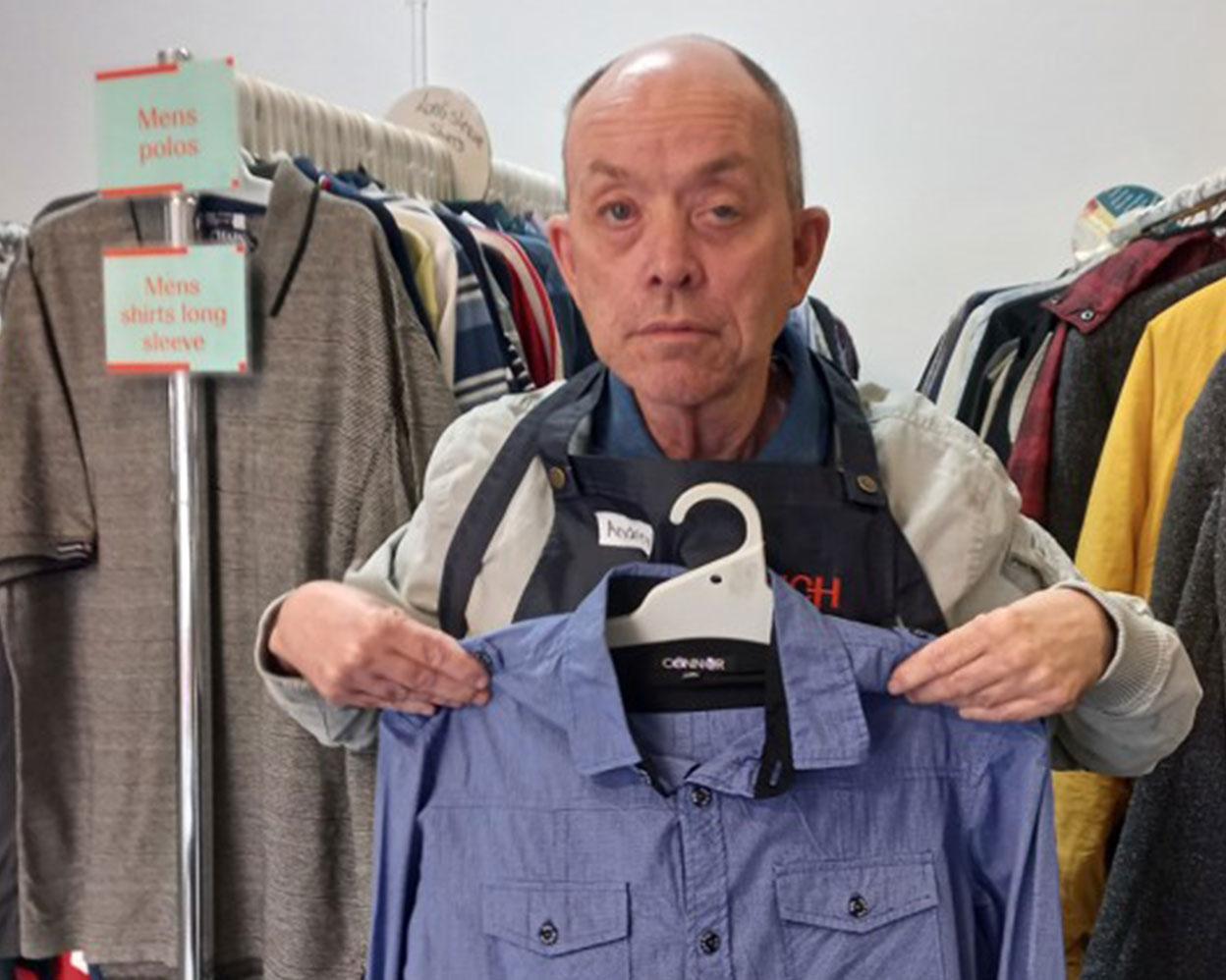 Man holding a shirt, while working at an Op Shop.