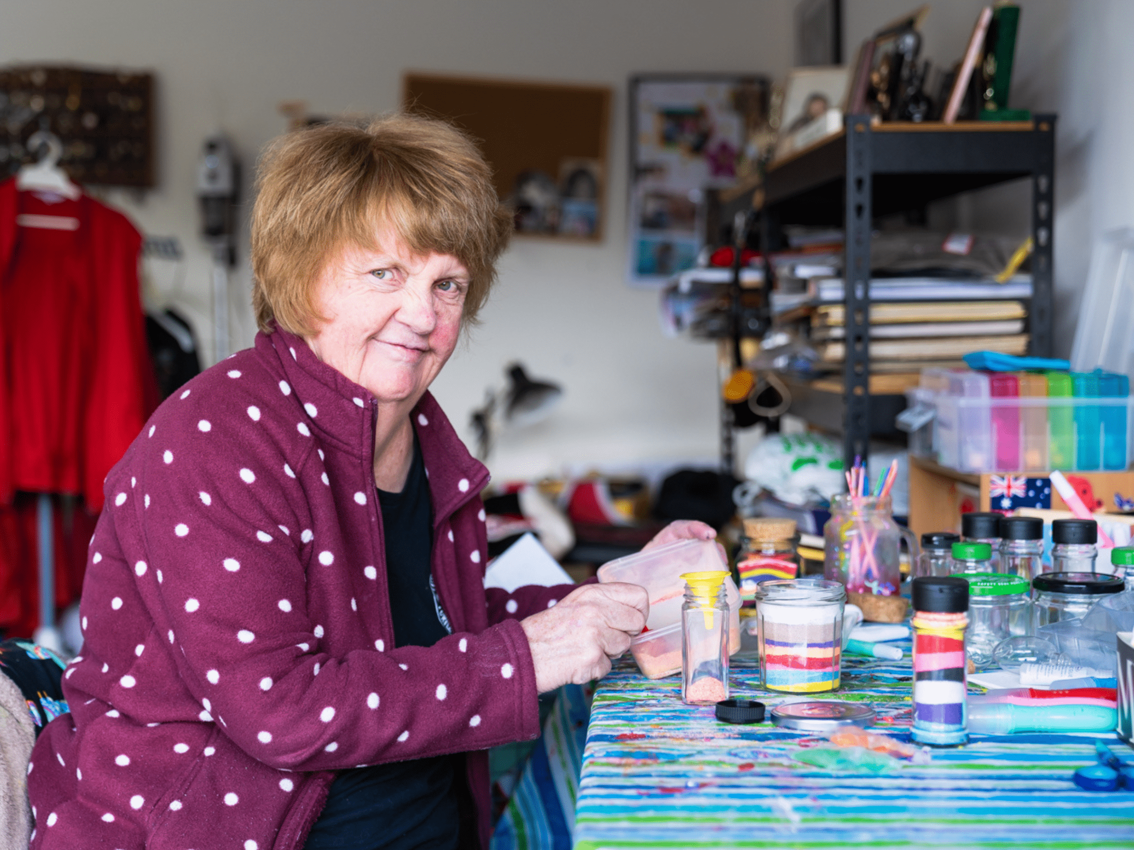 A woman in a purple and white polkadot top uses paints and smiles at the camera