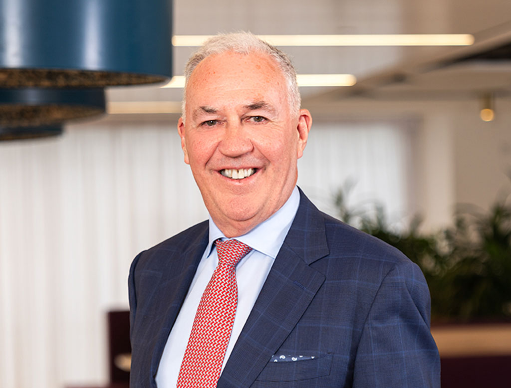 A man wearing a suit, standing in a corporate office, smiling.