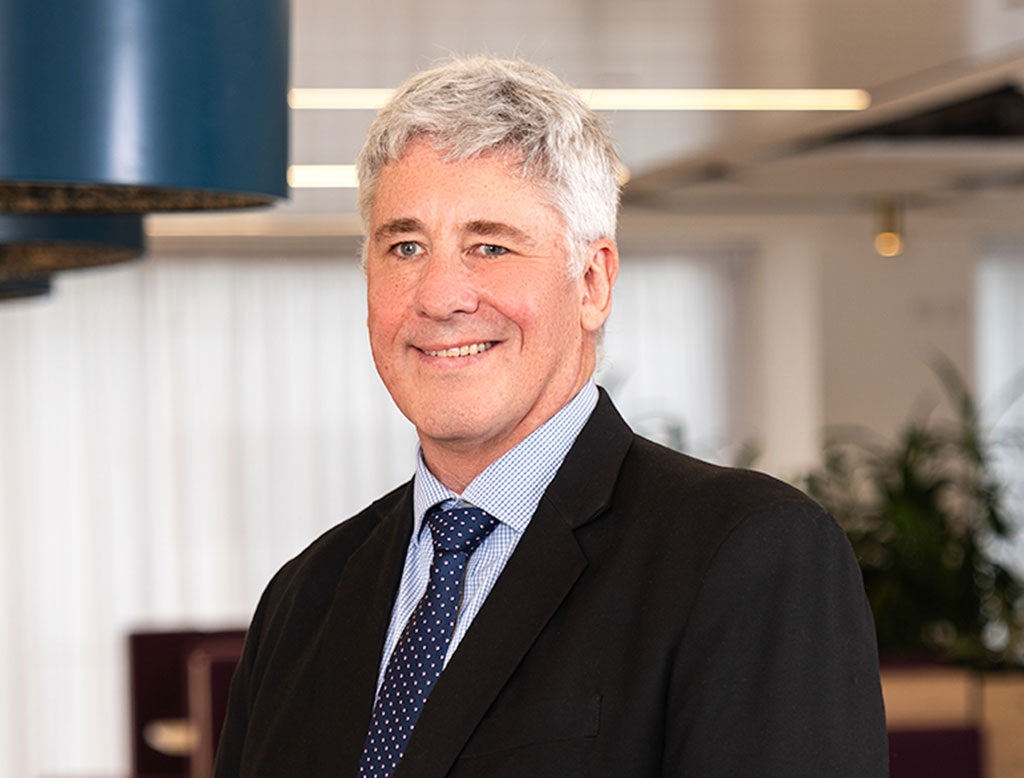 A man wearing a suit, standing in a corporate office, smiling.