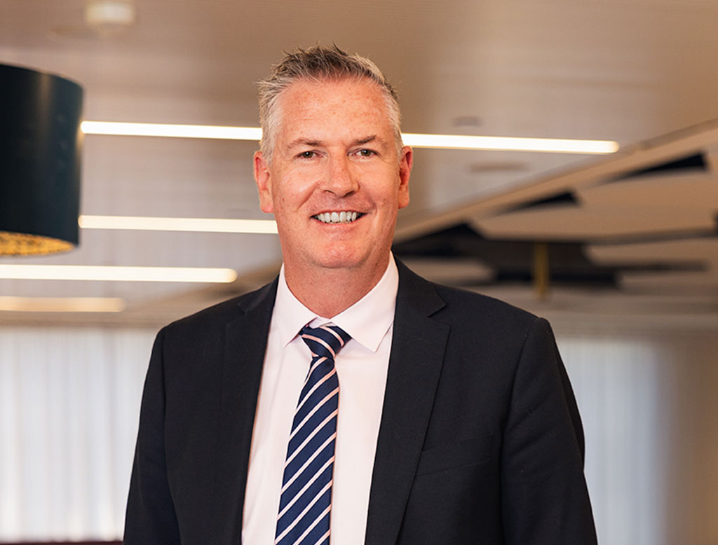 A man wearing a suit, standing in a corporate office, smiling.