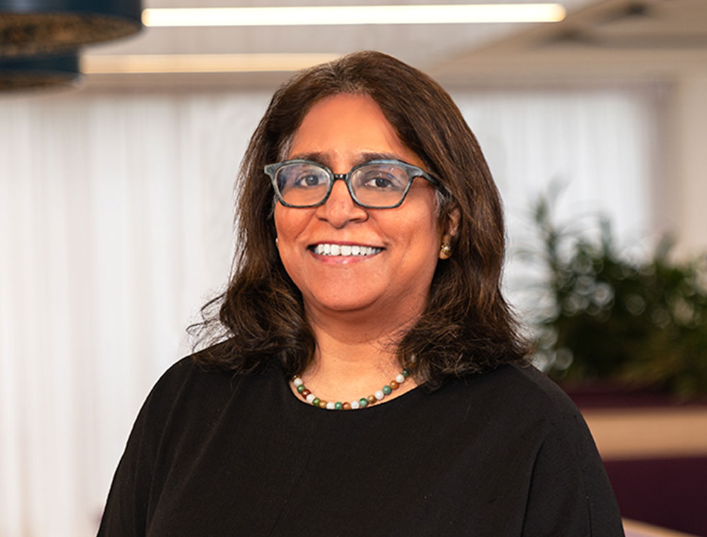 A woman wearing a black top, standing in a corporate office, smiling.