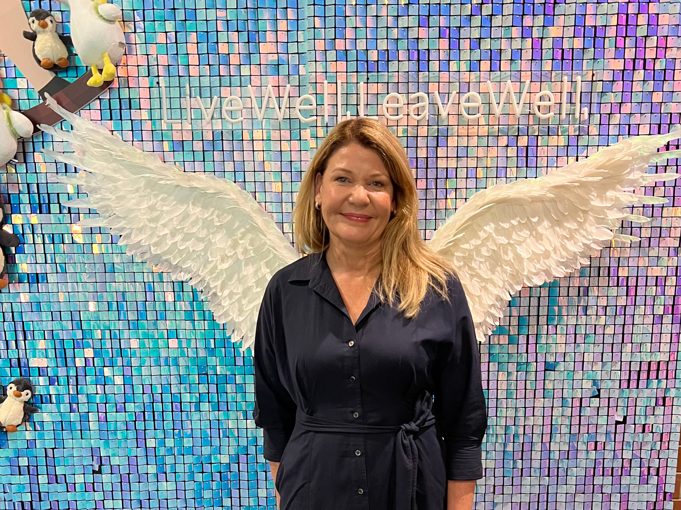 A woman stands in front of a wall that has painted on angel wings behind it