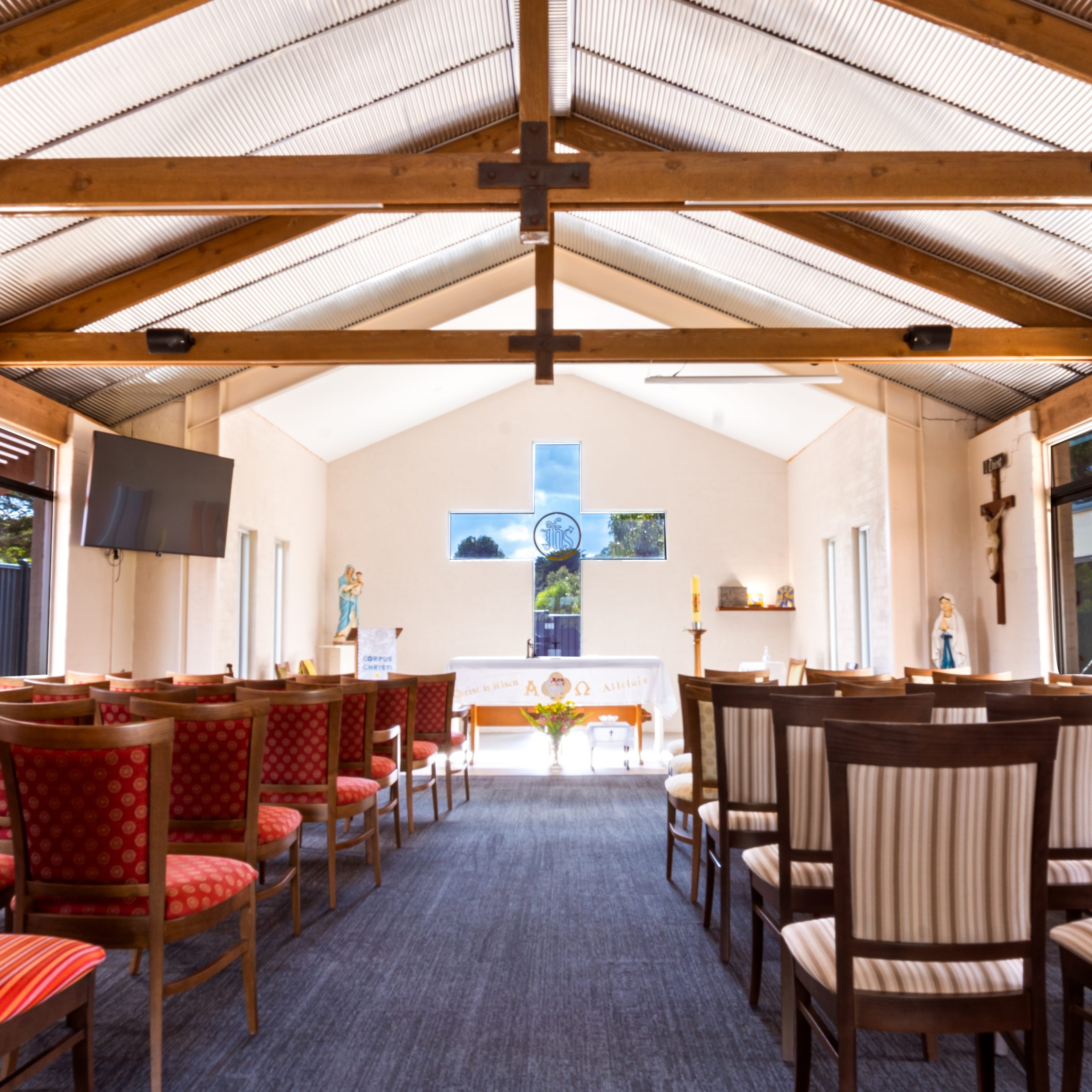 A chapel with high timber beams and chairs lined either side