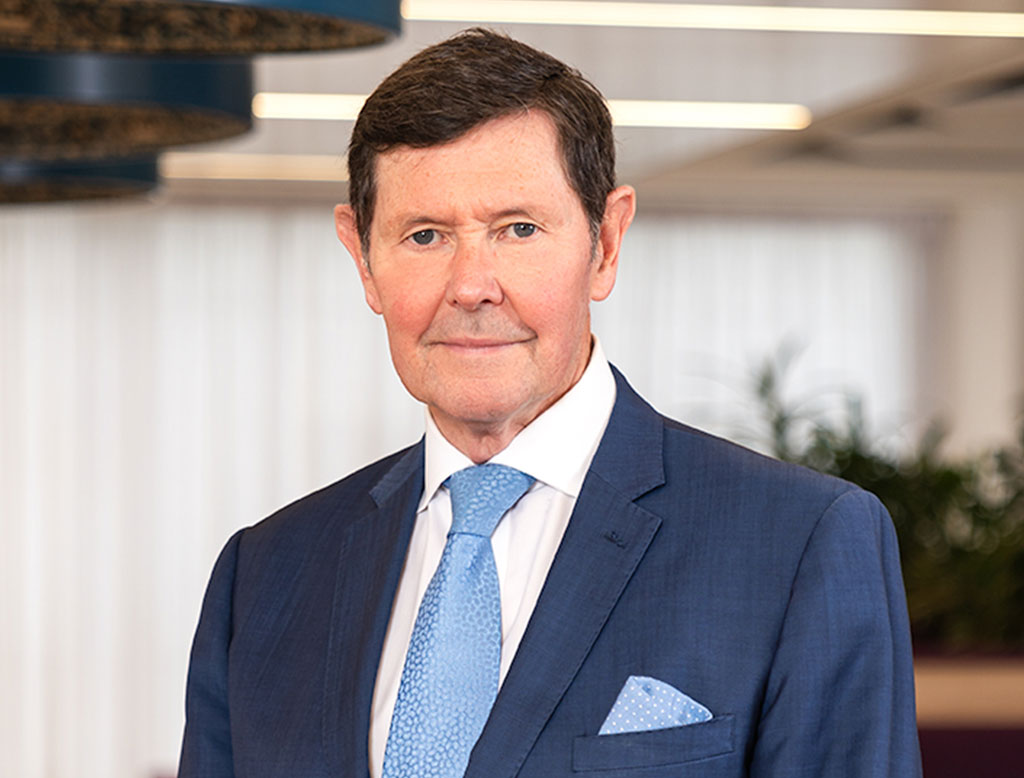 A man wearing a suit, standing in a corporate office, smiling.