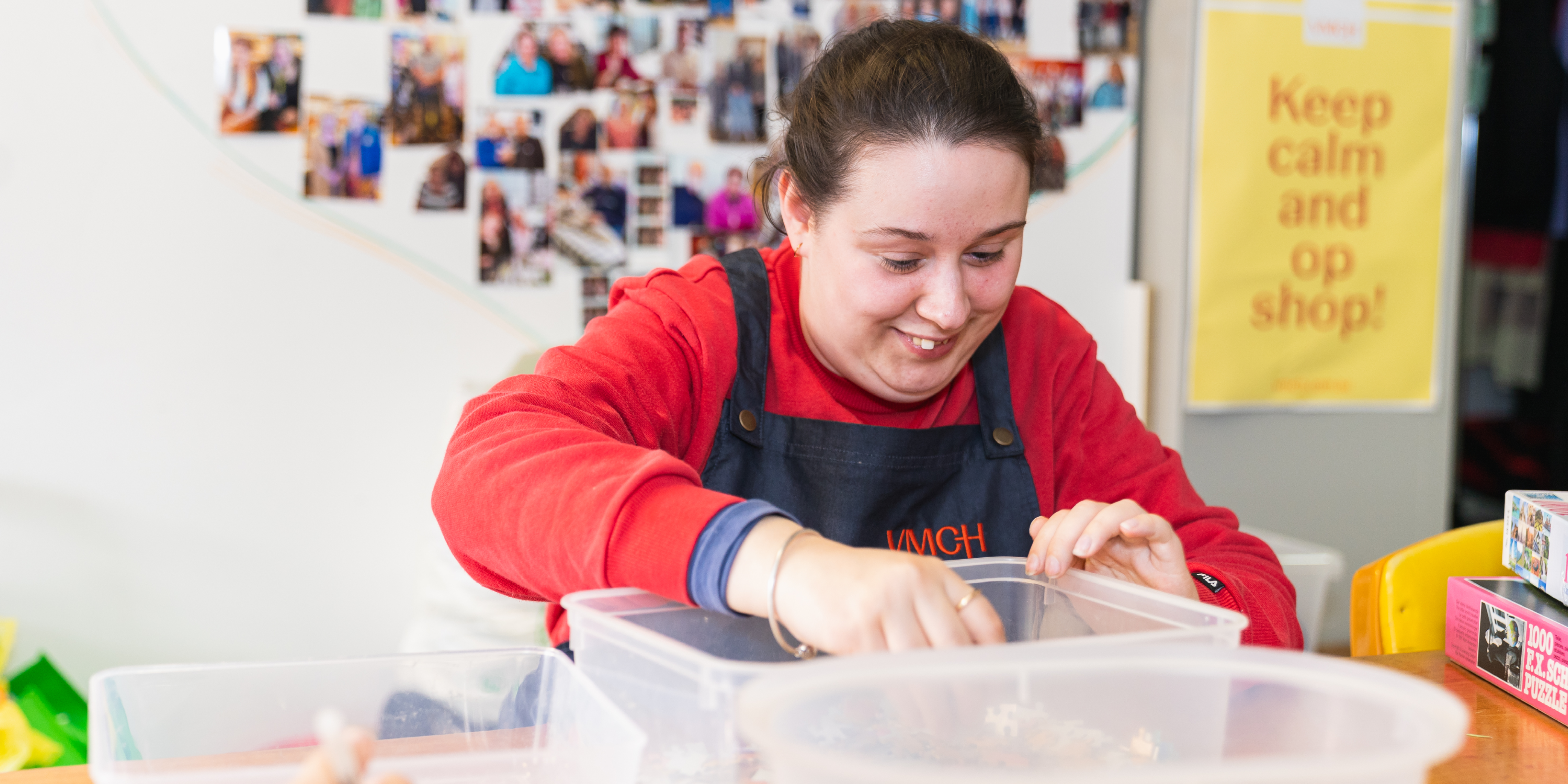 Woman wearing red top and apron sorting through buttons in plastic tub