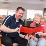 A middle aged man in and an older women sitting in a lounge room leaning over a document folder