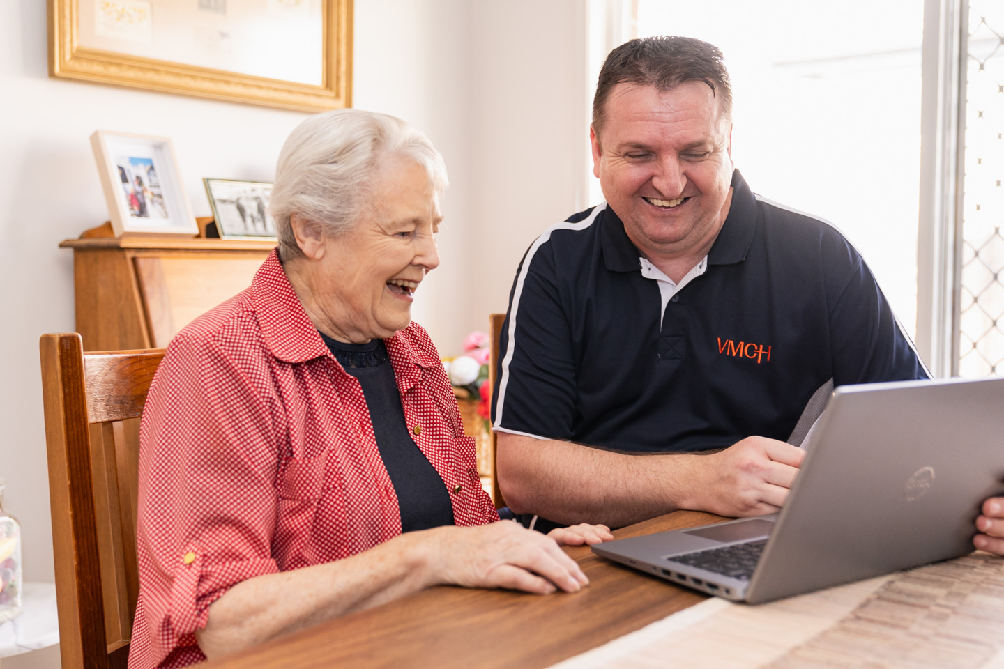 An older lady being shown something on a laptop by a Case manager at the kitchen table